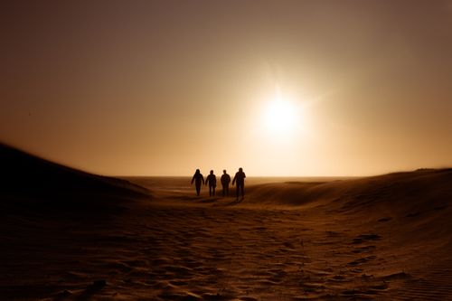 Free Silhouettes of people walking on sand dunes during a picturesque sunset in a desert landscape. Stock Photo