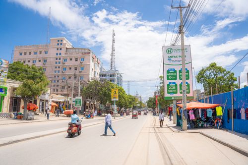 Free A vibrant street scene in Mogadishu, featuring local shops, pedestrians, and motorbikes under a clear blue sky. Stock Photo