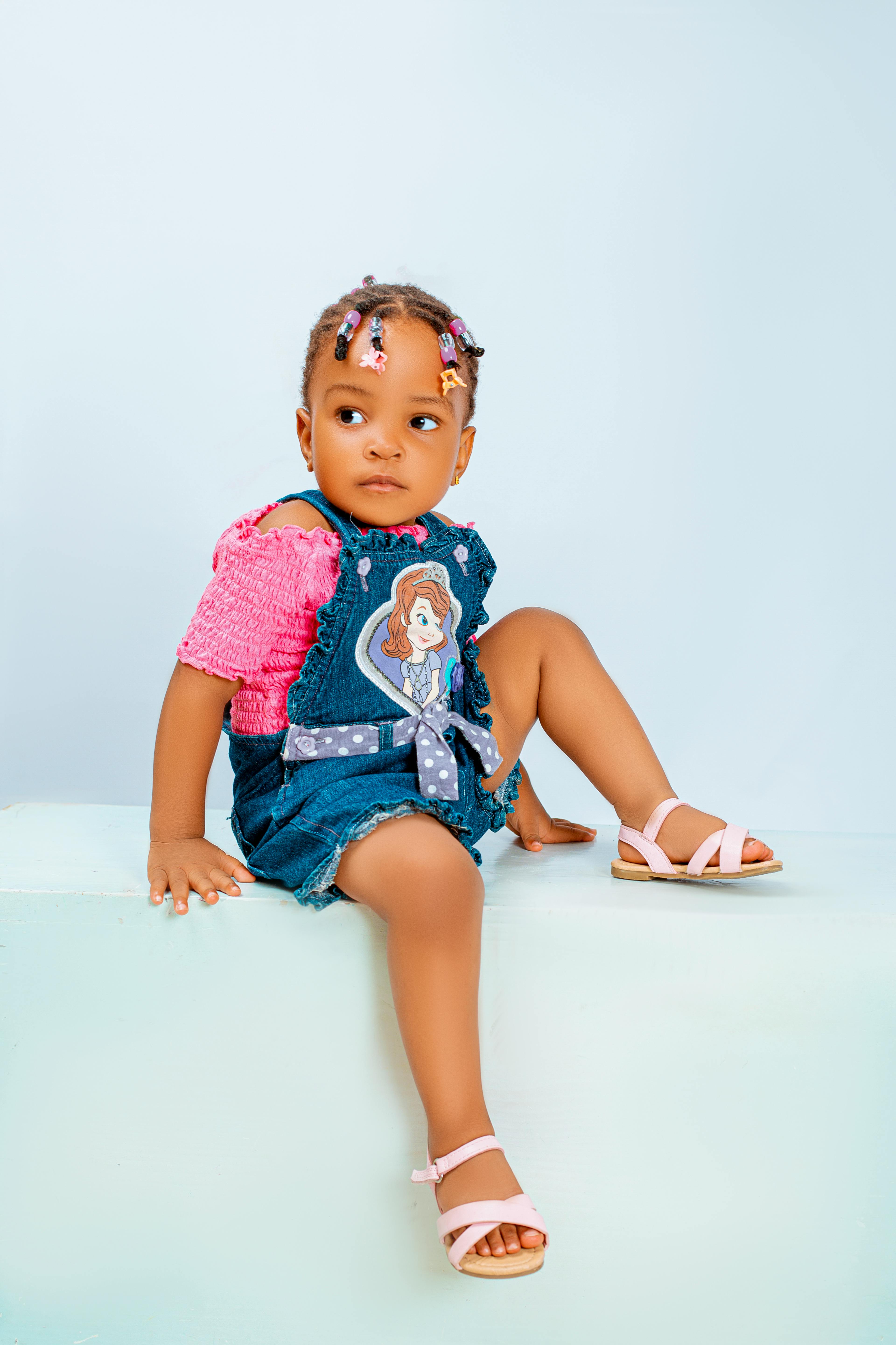 Charming photo of a toddler wearing a denim playsuit and pink top. Ideal for fashion or lifestyle themes.