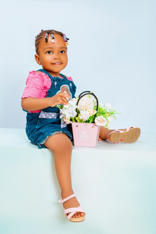 Free Charming portrait of a young child in a denim outfit holding flowers indoors. Stock Photo