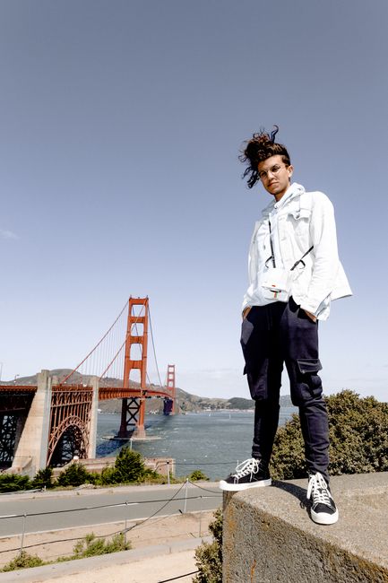 Stylish young man in denim jacket posing confidently by the iconic Golden Gate Bridge.