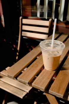 户外阳光明媚的木桌上，放着一个装有吸管的塑料杯