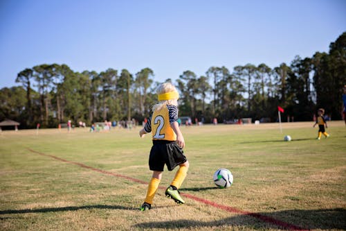 Boy Wearing Yellow and White Jersey Playing Soccer Field