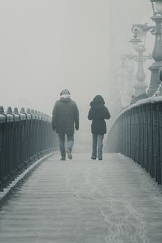 Two people walking on Liberty Bridge amidst fog in Budapest, creating a serene and mysterious ambiance.