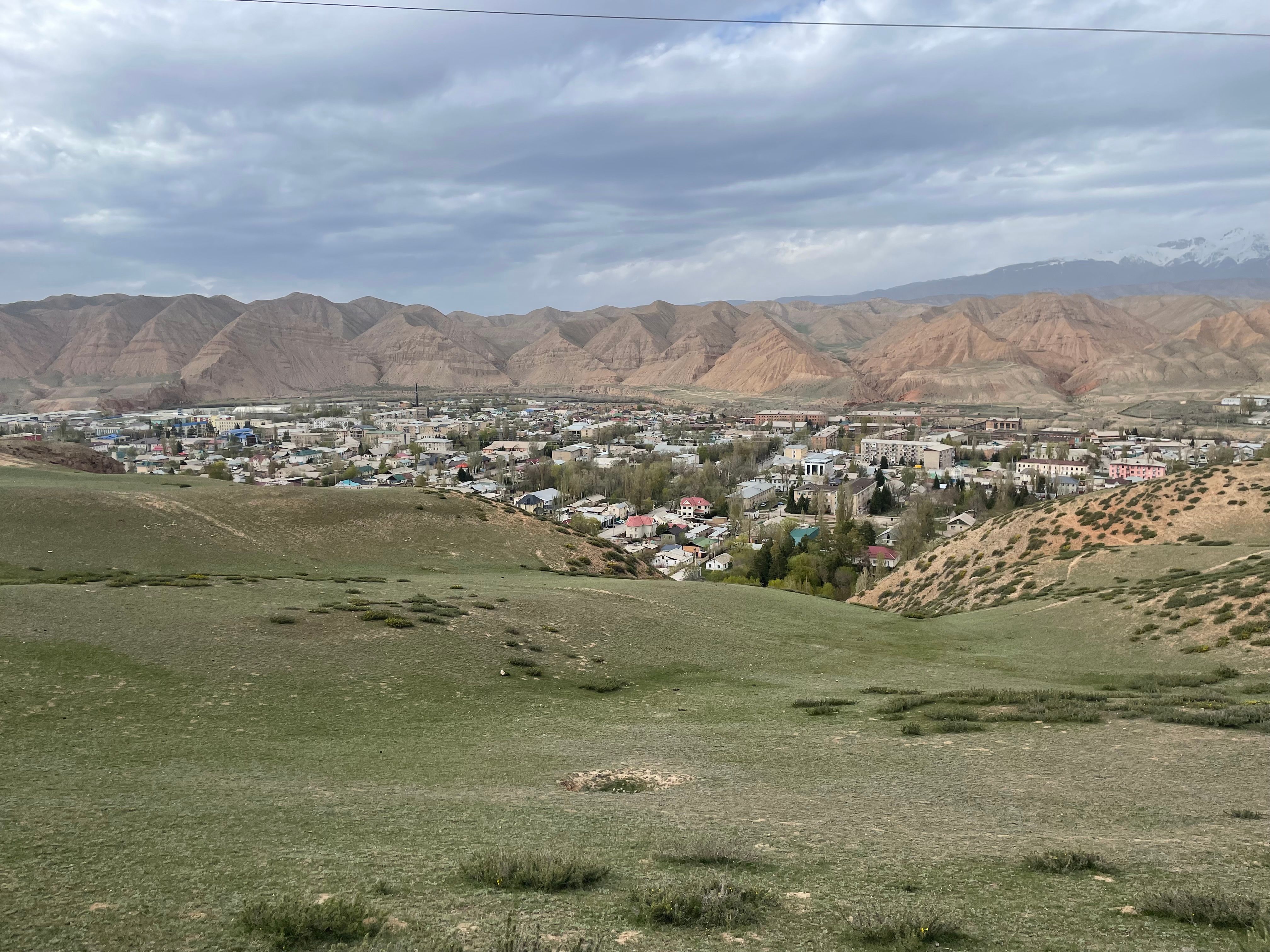 Une vue pittoresque de la ville de Naryn entourée de collines et de verdure sous un ciel nuageux.