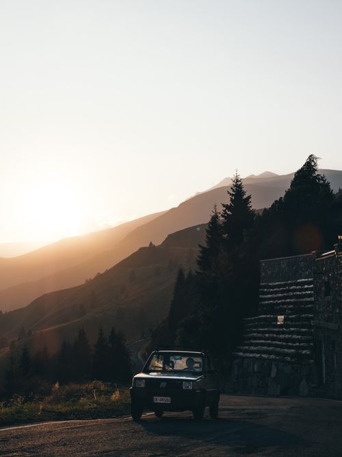 Free A vintage car drives along a scenic mountain road during a beautiful sunset. Stock Photo