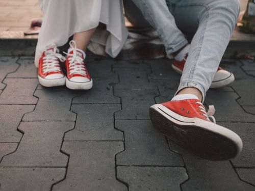 Free Two people wearing red sneakers sitting on urban pavement, showcasing casual and comfortable style. Stock Photo