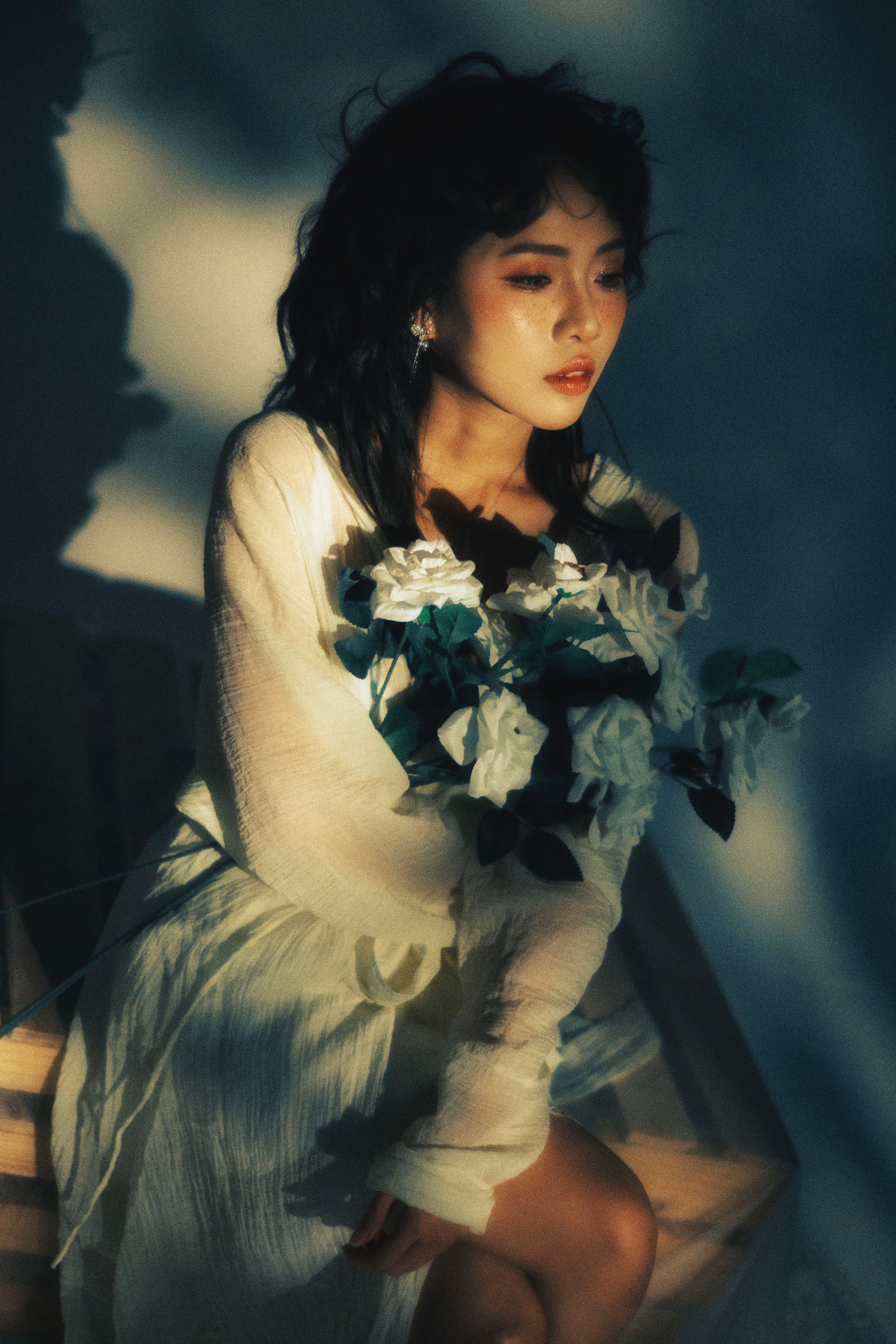 A serene portrait of an adult woman holding white roses, bathed in soft lighting.