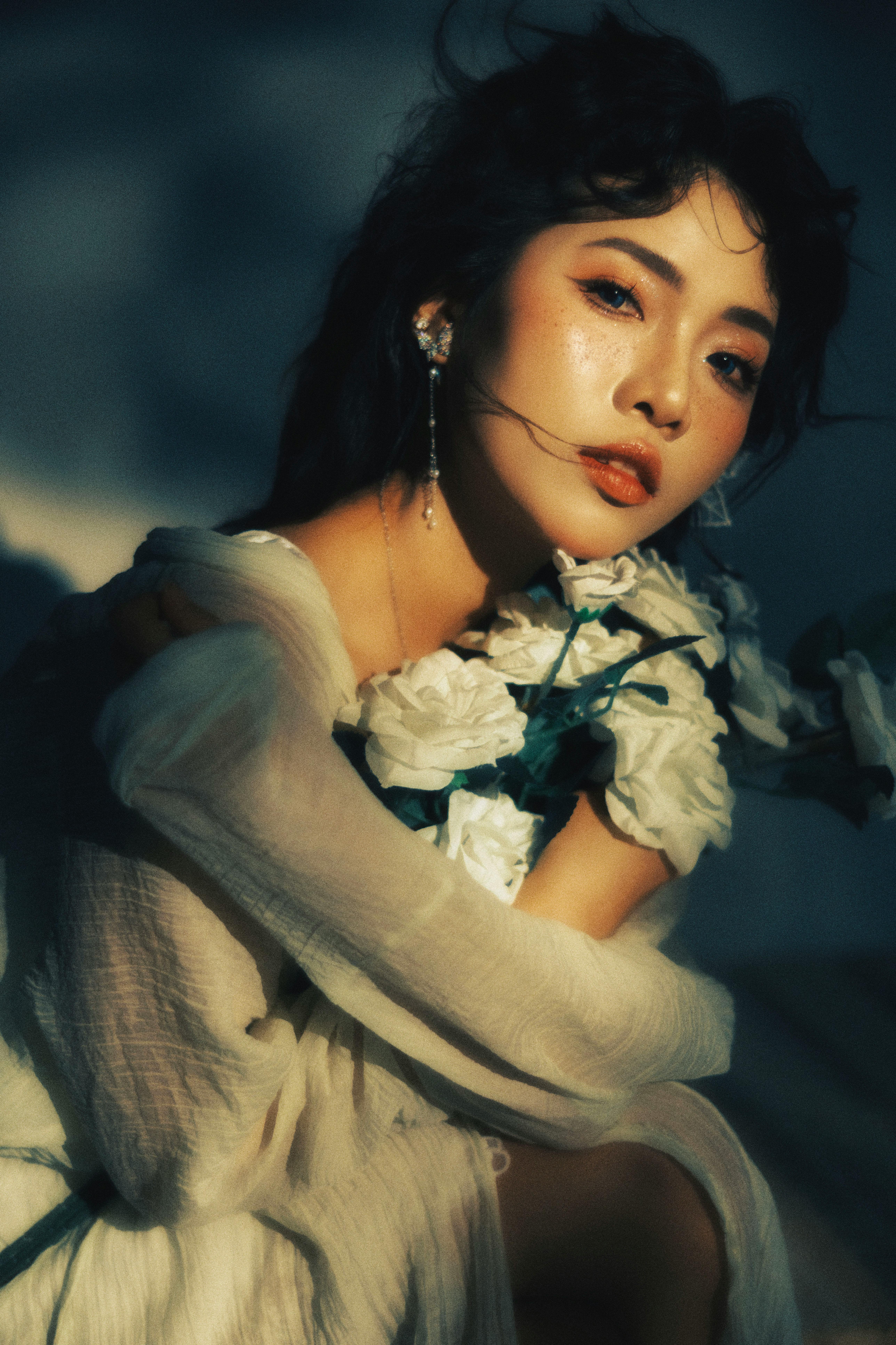 Artistic portrait of a woman with white flowers in a moody, soft light setting.