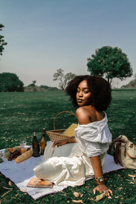A woman enjoys a serene picnic on a sunny day with wine and fruit.