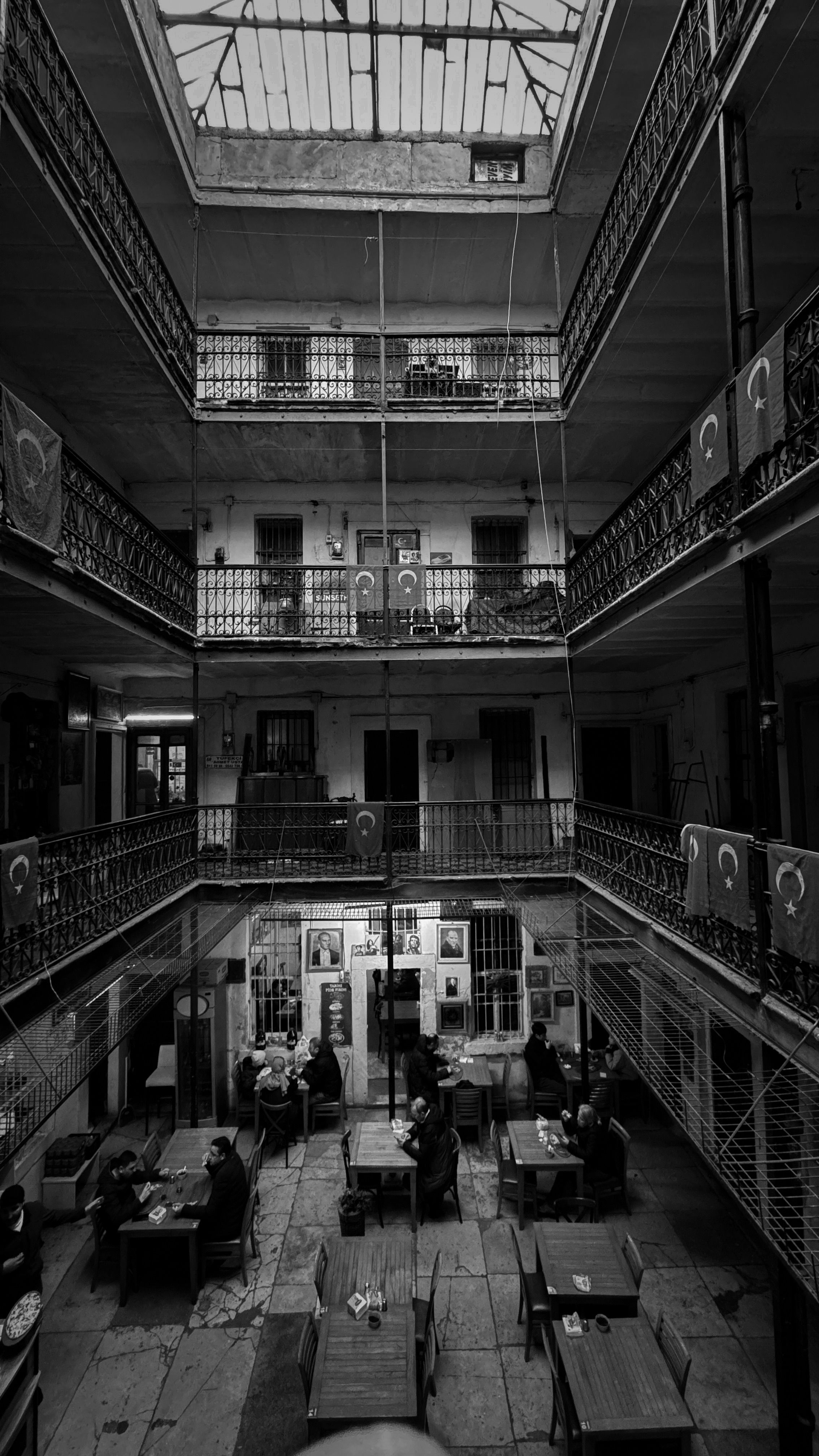 Black and white photo of a historic indoor atrium with Turkish flags and people.