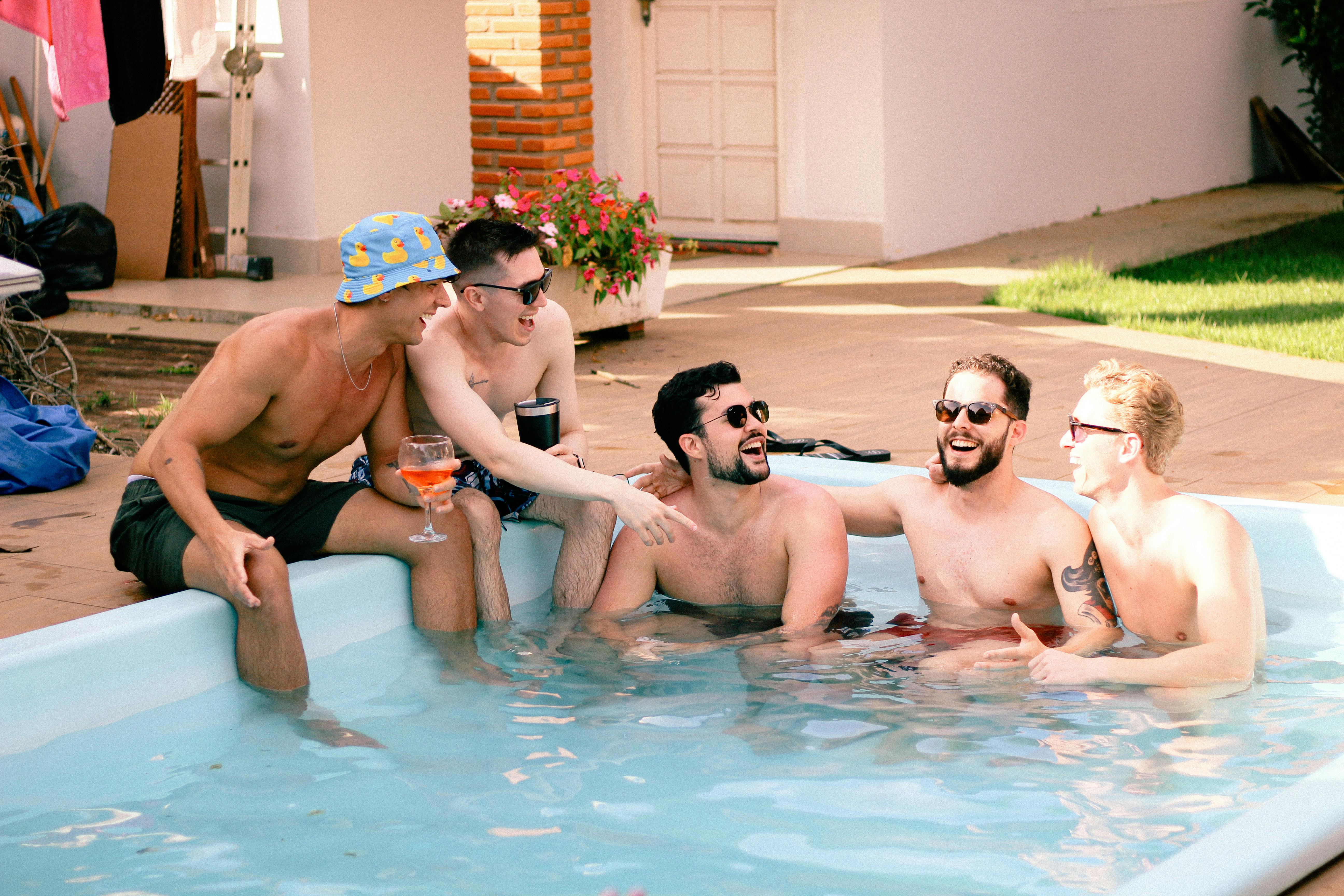 A group of men having fun and relaxing in a backyard pool under the sun.
