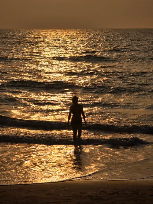 Free Silhouette of a person standing in ocean waves at sunset, creating a serene and reflective scene. Stock Photo