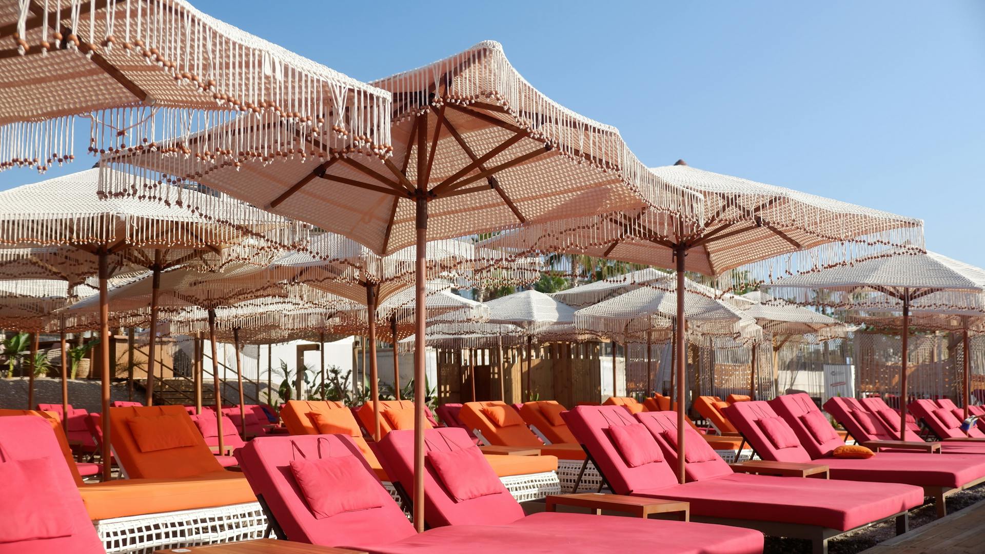 Vibrant beach loungers under decorative parasols on a sunny day, perfect for relaxation and leisure.