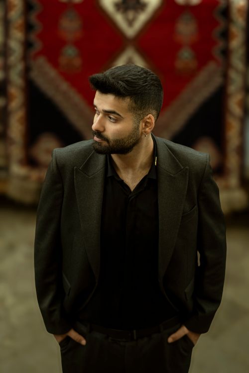 Free Portrait of a fashionable man in a black suit with a vibrant woven background in Tehran, Iran. Stock Photo
