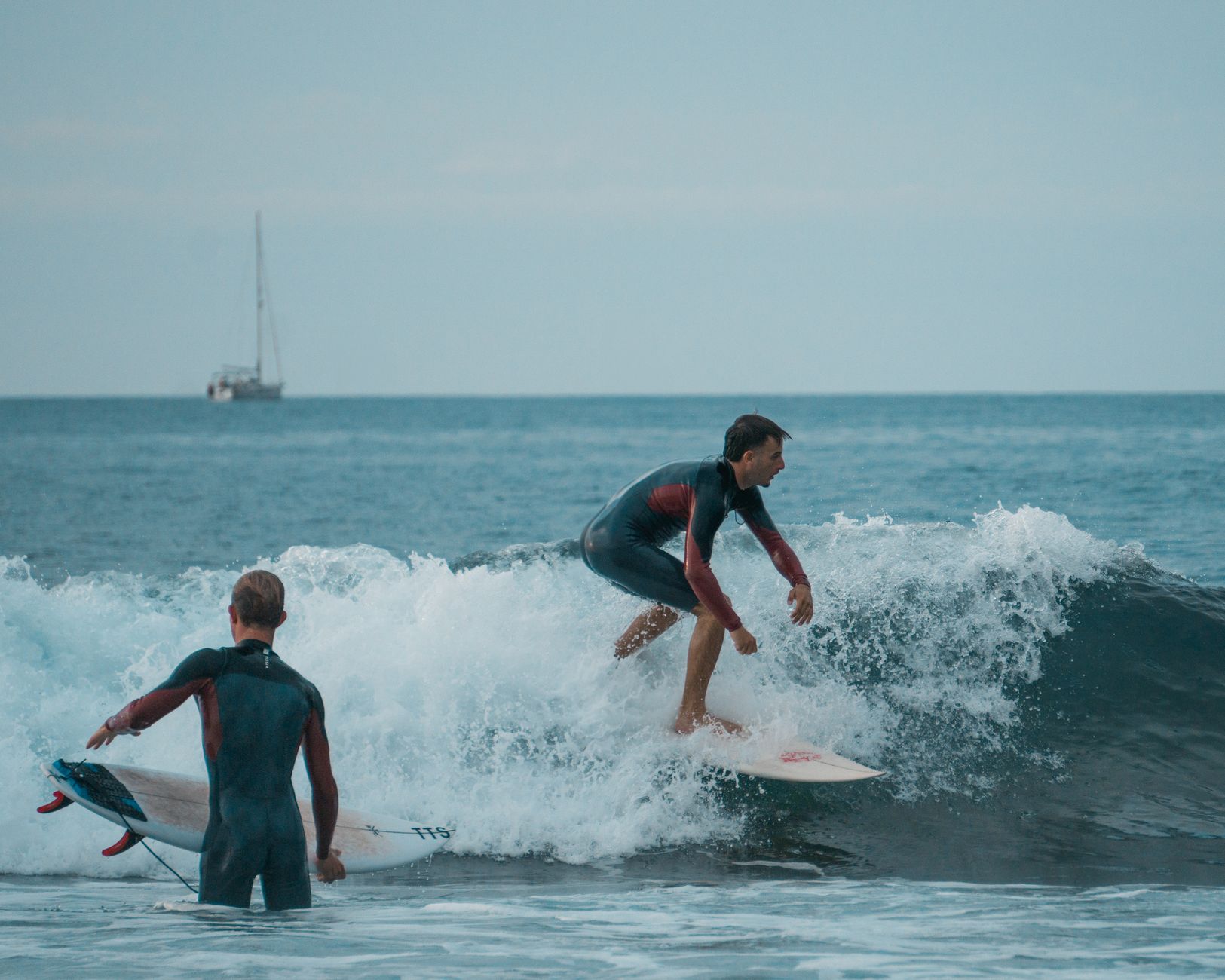 Two young men surfing on a wave in an open ocean setting, capturing the thrill of the sport.