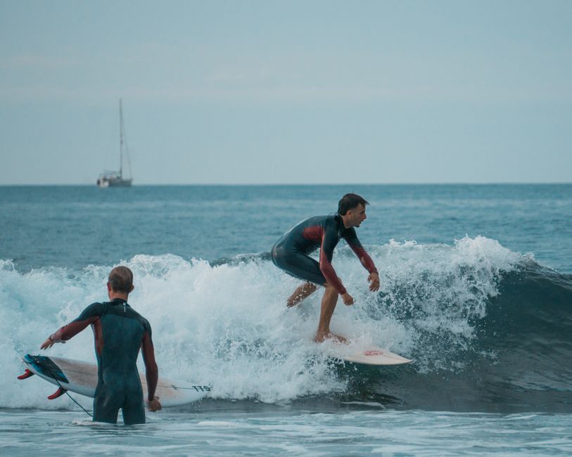 Two young men surfing on a wave in an open ocean setting, capturing the thrill of the sport.
