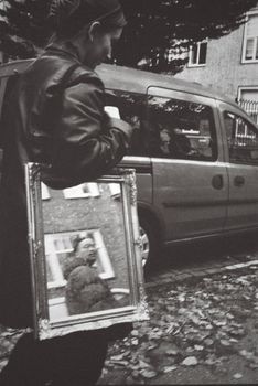 Black and white photo of a woman reflecting in a mirror on a city street.