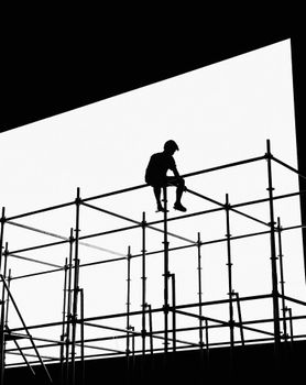 Dramatic black and white silhouette of a worker sitting on scaffolding.