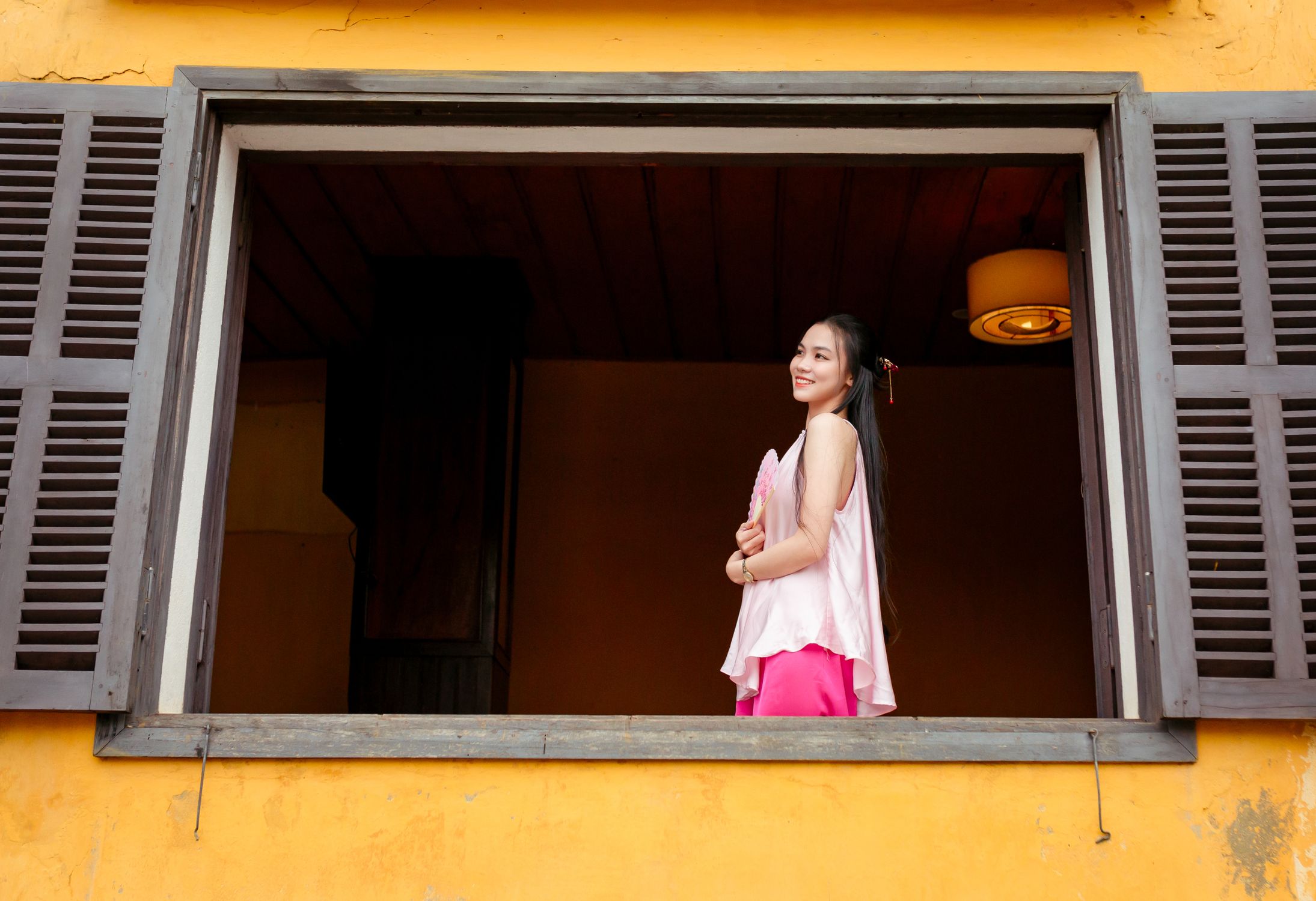 Woman in Vietnamese attire stands smiling in a window, Hoi An.