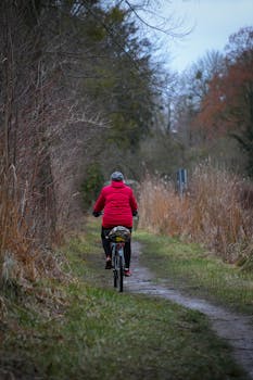 Person cycling on a winter trail surrounded by nature, wearing winter gear for warmth.
