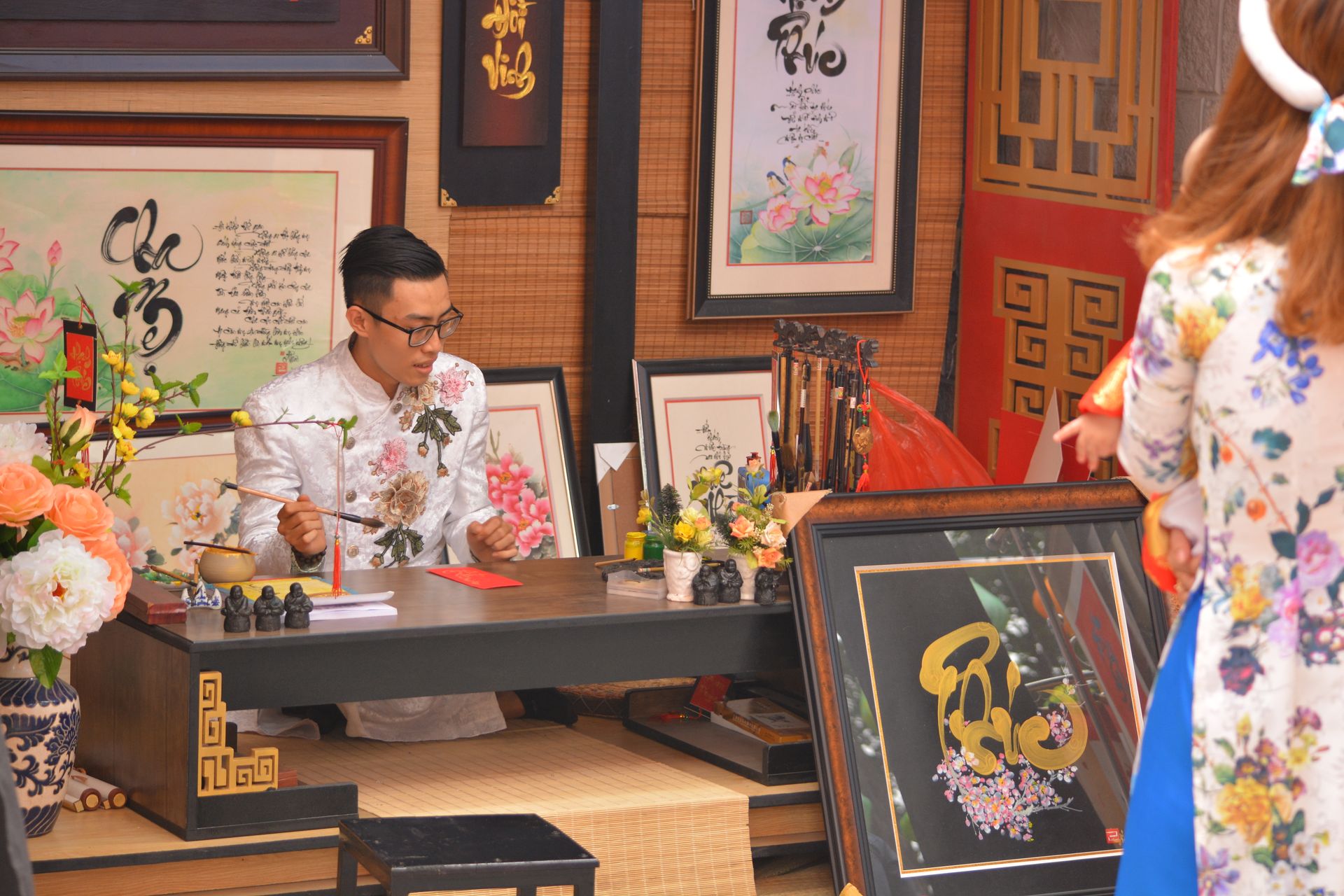 Image of a traditional Asian art shop with an artist at work amidst floral decorations and framed paintings.