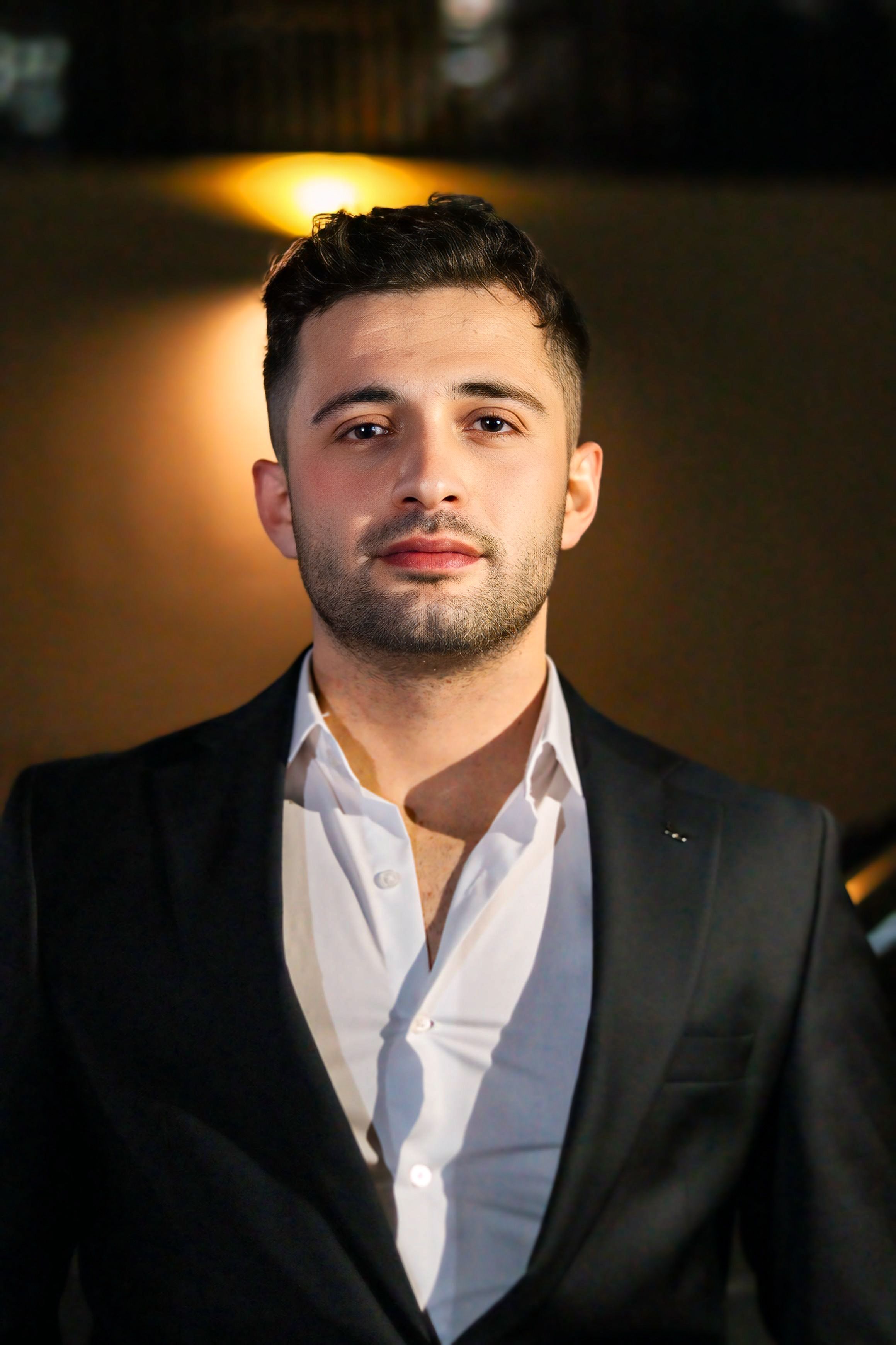 Portrait of a confident young man in a suit at night with a warm background glow.