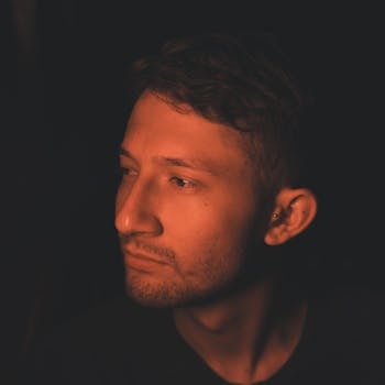 Close-up portrait of a man bathed in warm, dramatic lighting, creating a moody atmosphere.
