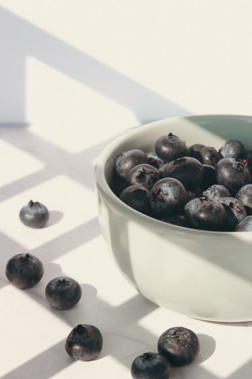 Free A ceramic bowl filled with juicy blueberries placed in bright natural sunlight casting shadows. Stock Photo