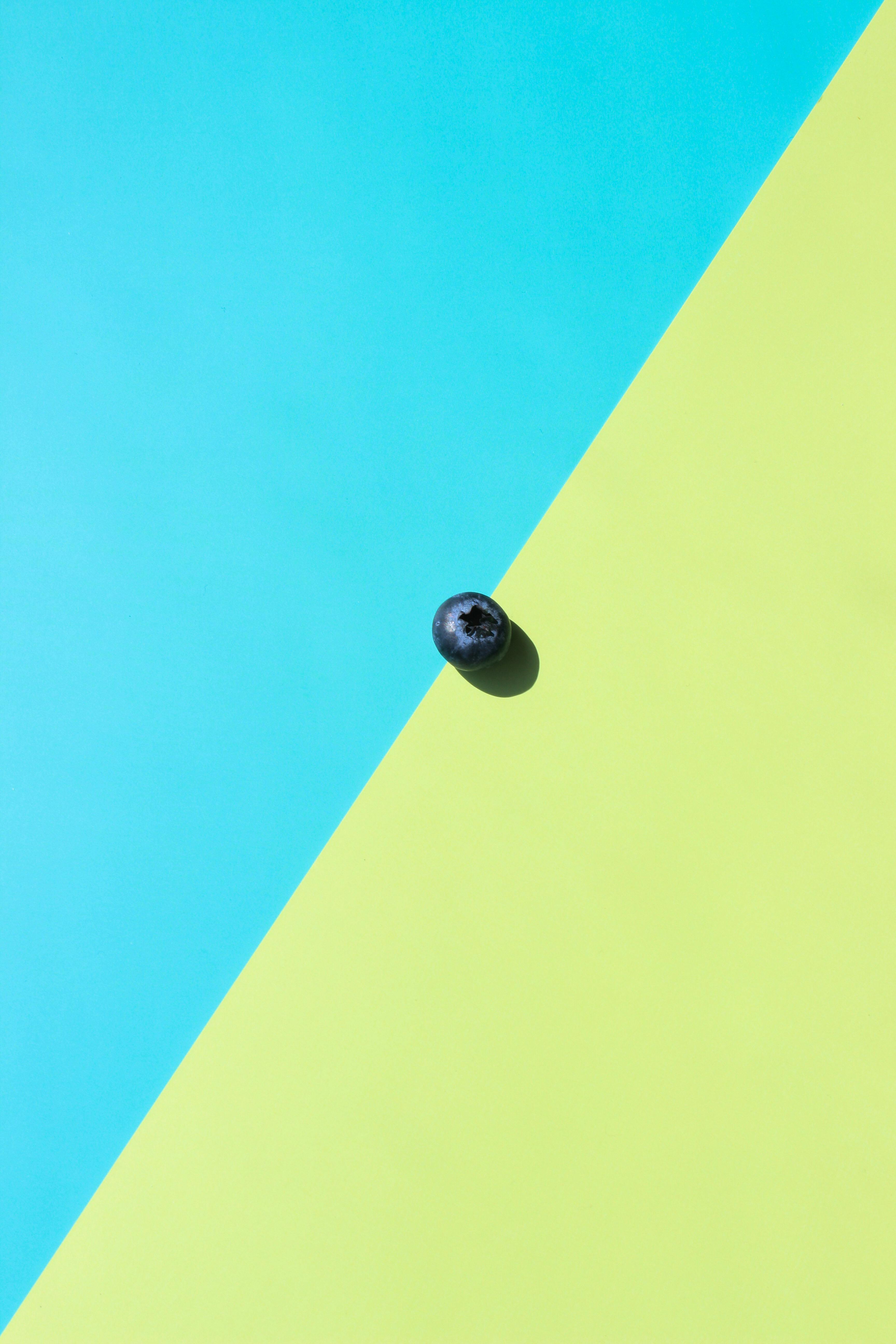 gratis Een enkele bosbes op een diagonale blauw-groene achtergrond, wat het contrast benadrukt. Stockfoto