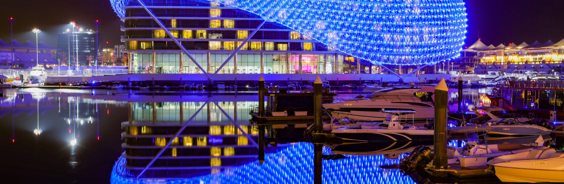 Modern hotel with vibrant blue lights reflecting in calm waters at night.