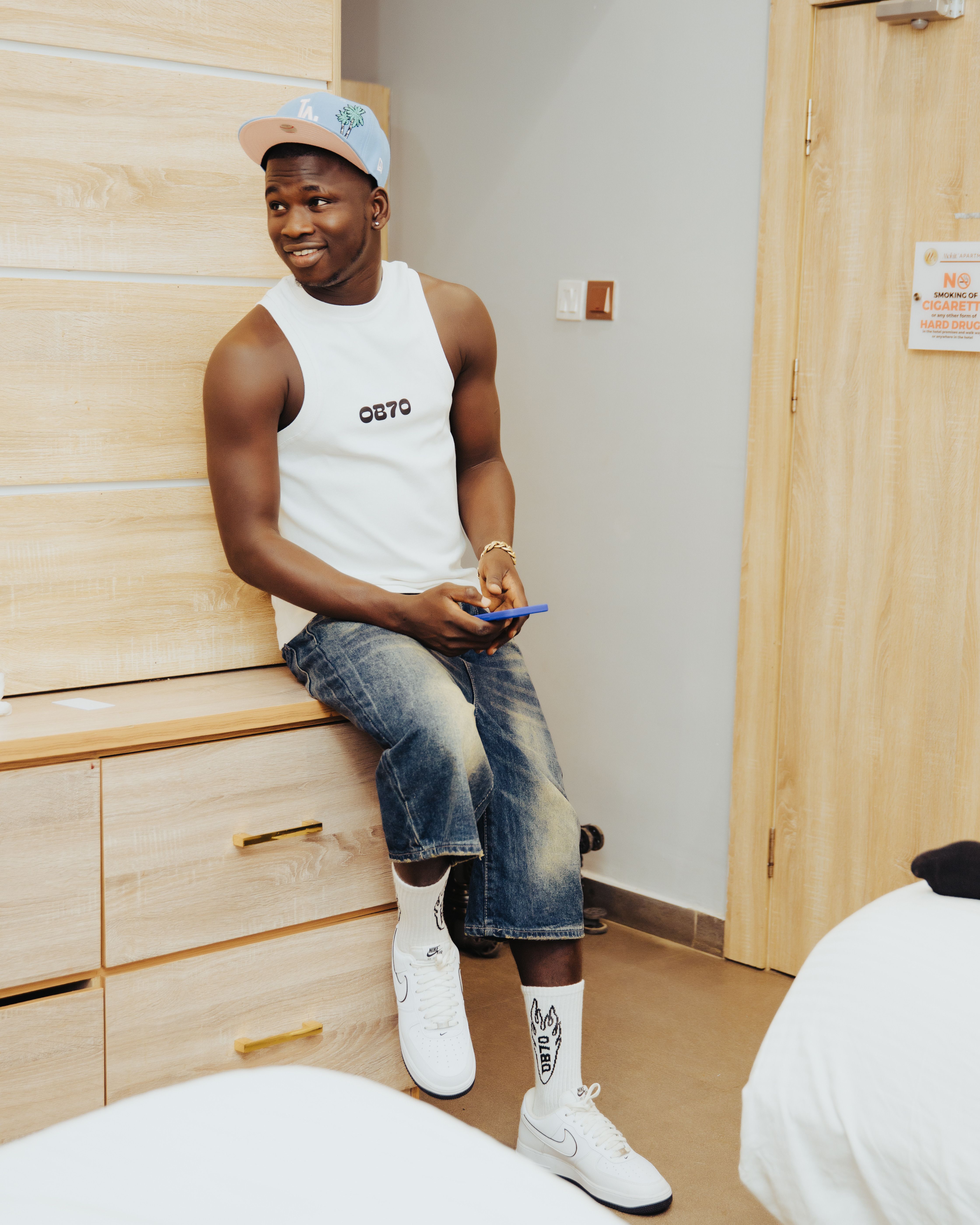 Young man in trendy streetwear sitting indoors, looking relaxed and cheerful.