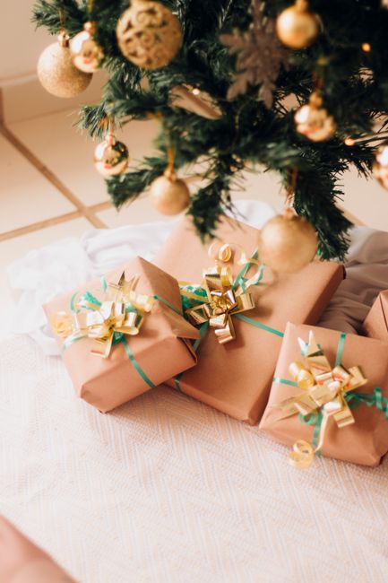 Beautifully wrapped presents with golden bows under a decorated Christmas tree.
