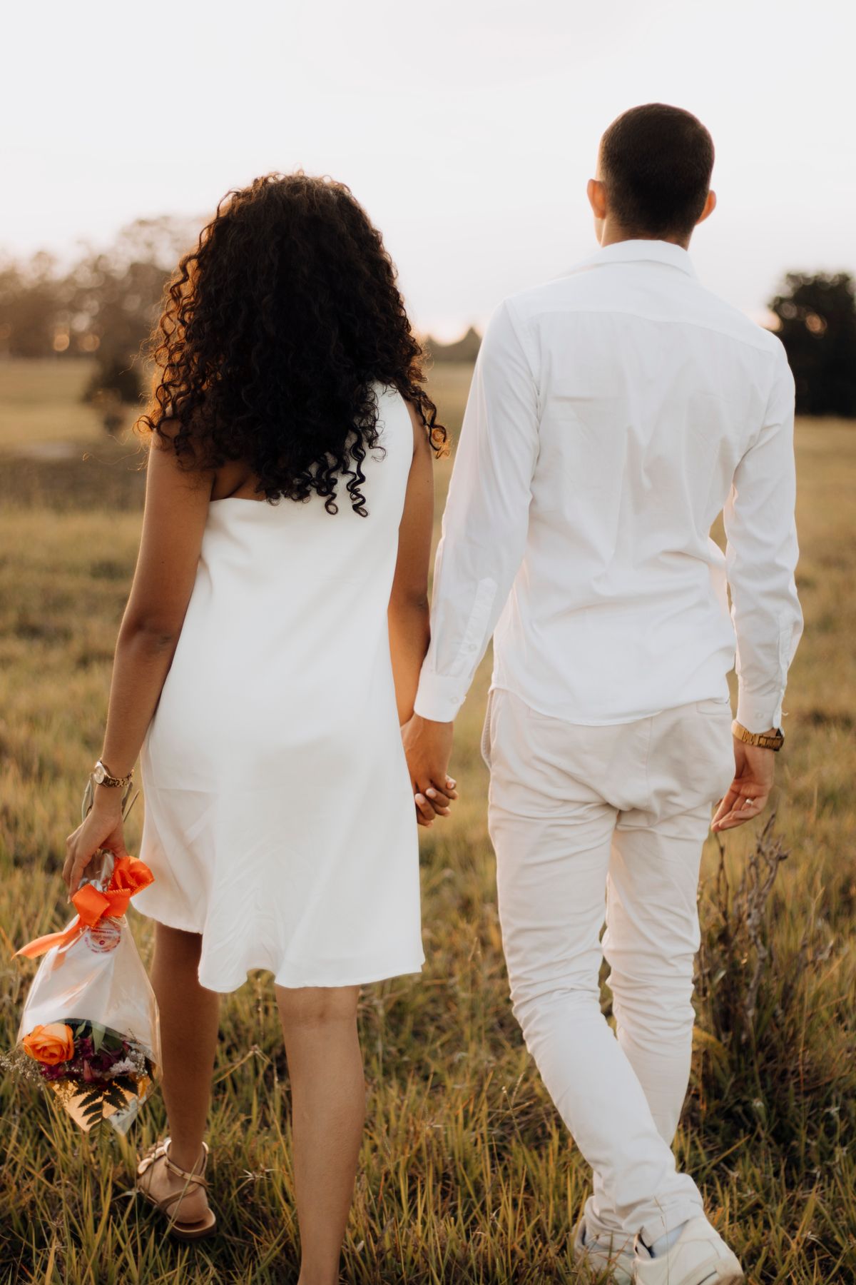 Couple walking hand in hand through a field at sunset