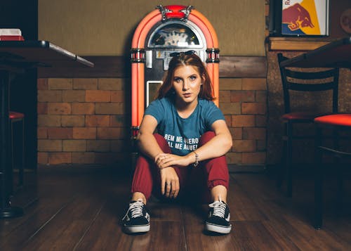 Free Woman Wearing Blue Shirt and Red Track Pants Sitting Beside of Jukebox Stock Photo