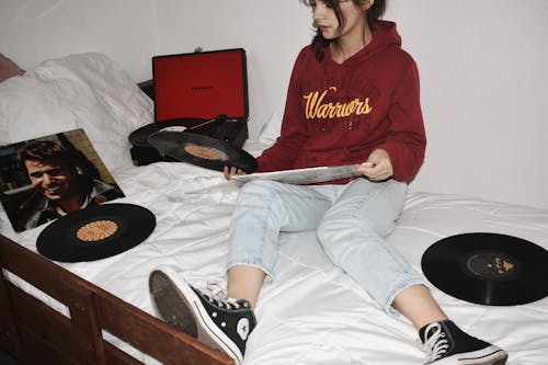 Free Woman Sitting on Bed Holding Vinyl Records Stock Photo