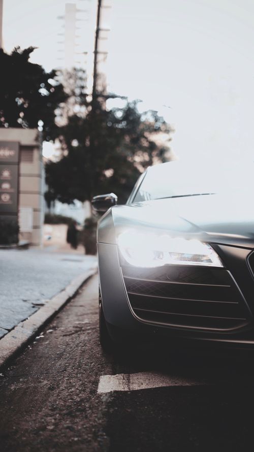 Free Close-up of a sleek modern car with headlights on, parked on a city street at dusk. Stock Photo