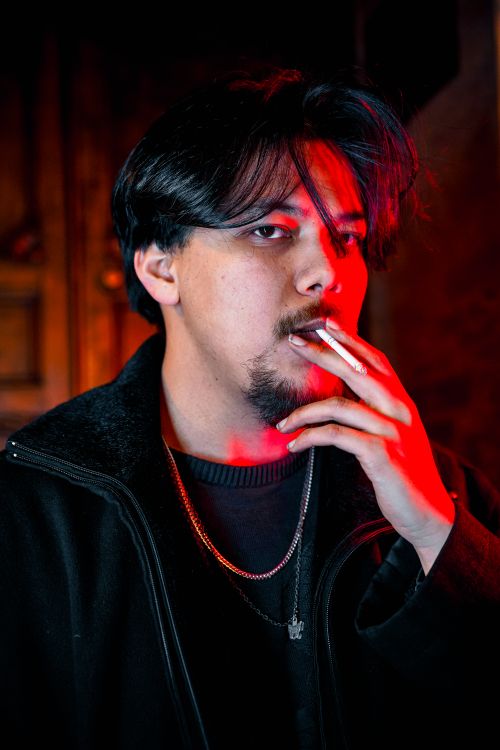 Free Portrait of a young man smoking a cigarette in dramatic red and blue lighting. Stock Photo