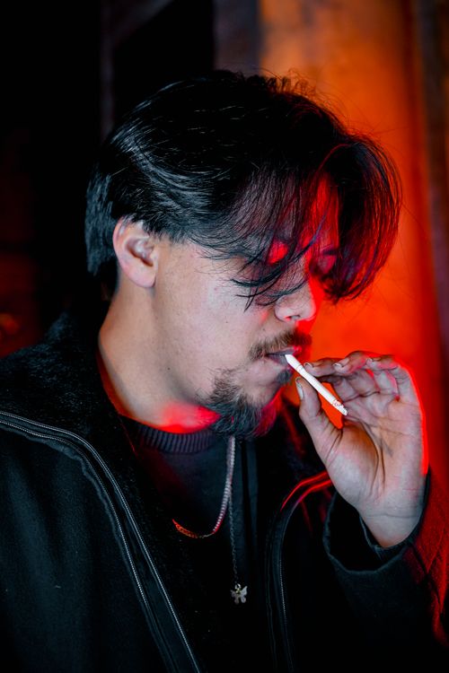 Free Close-up of a man smoking a cigarette with intense red lighting, creating a dramatic mood. Stock Photo