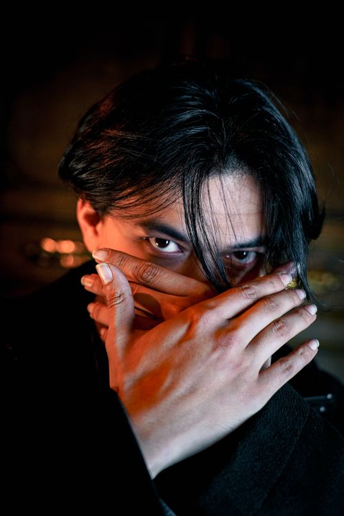 Free Intriguing portrait of a man partially hiding his face with his hand in a dimly lit setting. Stock Photo