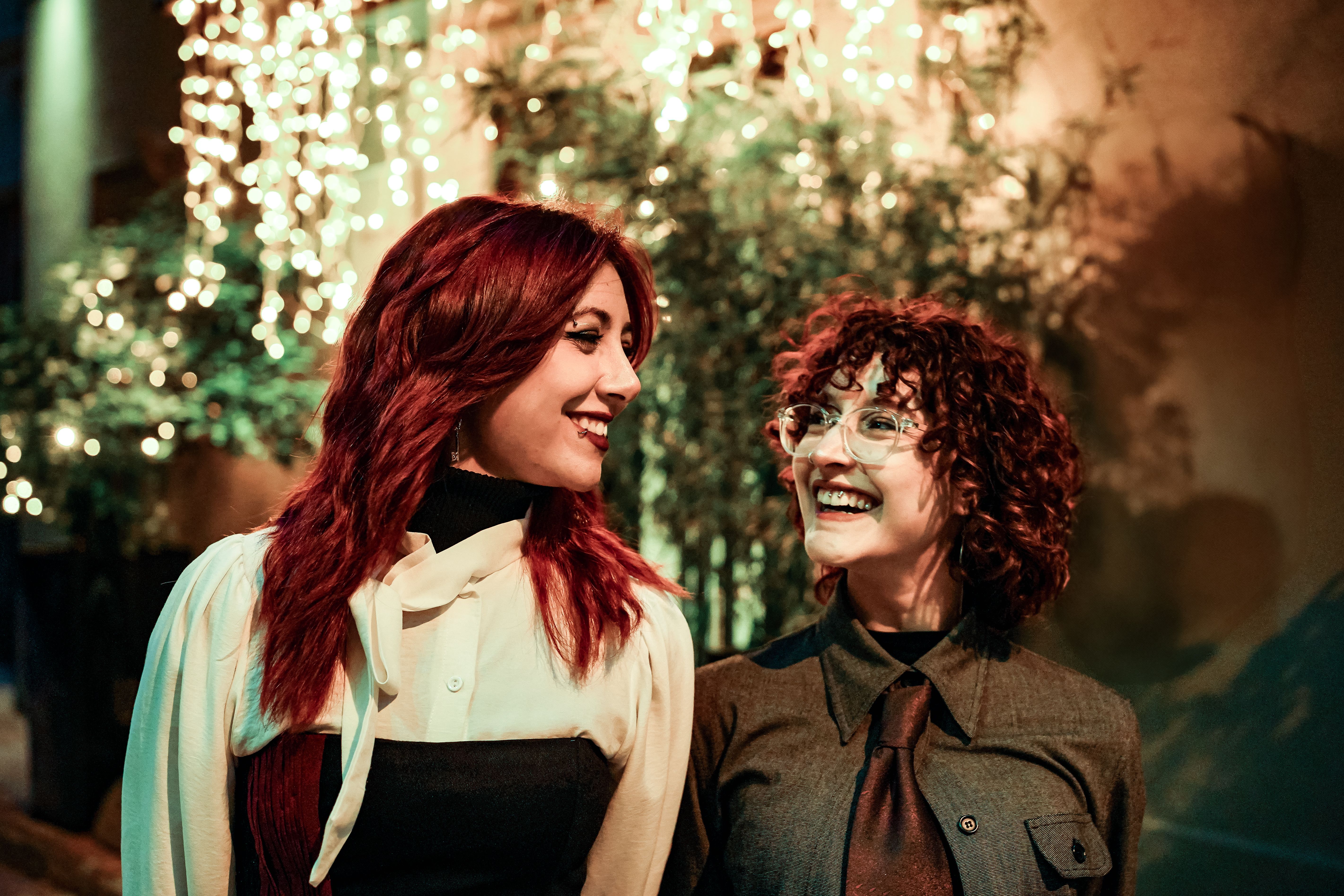 Two women enjoying a night out illuminated by warm, festive lights, creating a joyful ambiance.
