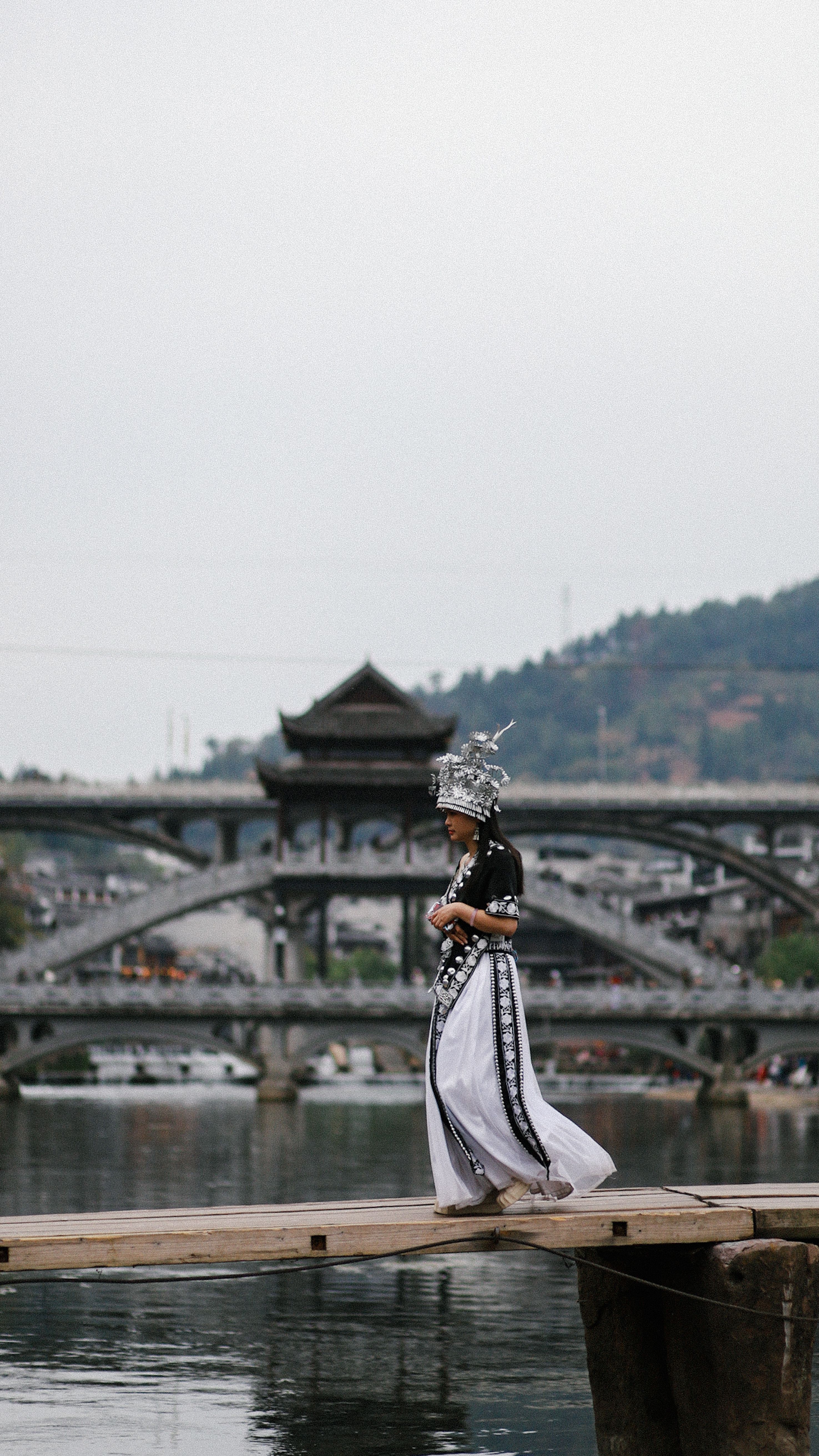 Woman in traditional attire walking on a bridge with a scenic backdrop.
