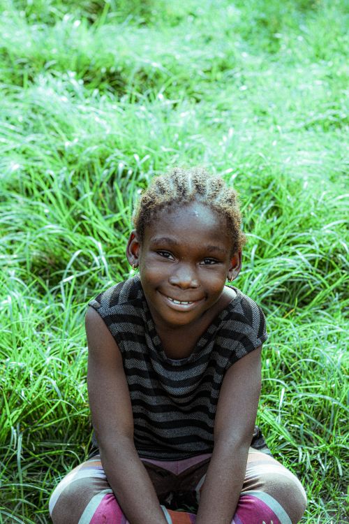 Free Joyful child sitting amidst lush grass, radiating happiness and innocence in a natural setting. Stock Photo