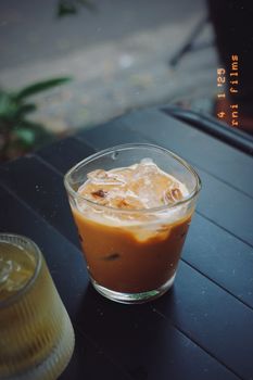 Chilled iced coffee in a clear glass on a black outdoor table with a vintage film effect.