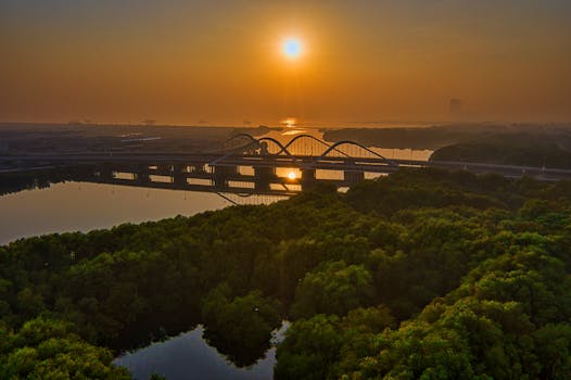 日落时分，从空中俯瞰雅加达的一座桥梁，水面倒影与四周郁郁葱葱的绿色植物构成了一幅令人惊叹的画面