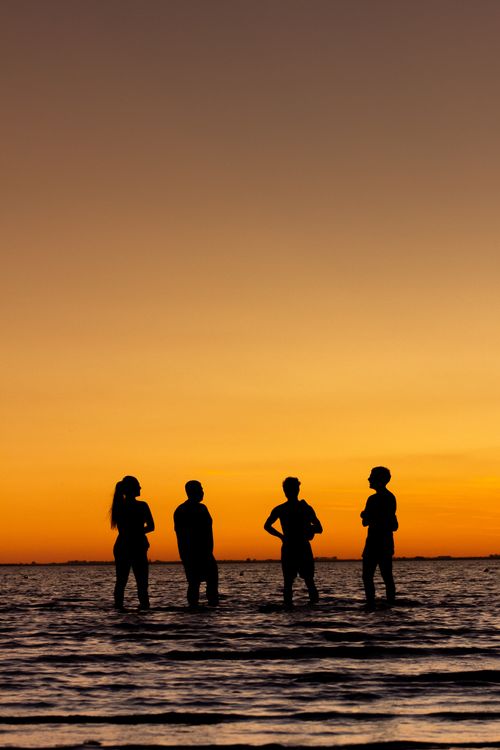 Free Silhouettes of four people standing in the water against a vibrant sunset in Carreras, Argentina. Stock Photo