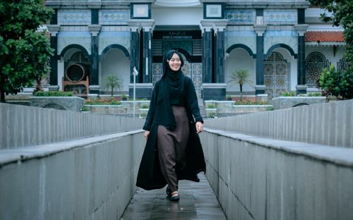 Free Woman in traditional attire walks near a grand architectural building, showcasing cultural beauty. Stock Photo
