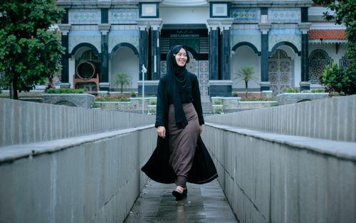 Free Young woman in a hijab smiling as she walks in an architectural setting. Stock Photo