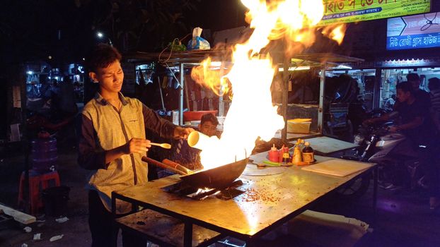 Dramatic street food scene with a vendor cooking using high flames at a night market.