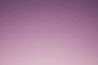 黄昏时分，淡紫色的天空宁静柔和，一架小飞机和一弯新月点缀其中